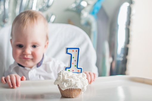 Cute toddler boy for first year of birth eating birthday cupcake with 1 candle close-up and copy space.