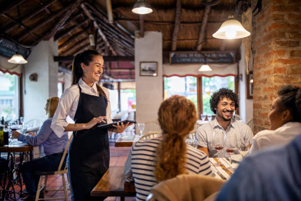 Restaurant waitress taking lunch order from guests Smiling waitress using a digital tablet while taking lunch order from guests sitting at a restaurant table. Woman working at a restaurant taking order from a group of people. waitress stock pictures, royalty-free photos & images