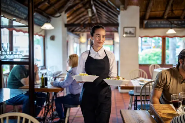 Waiter walking holding two dishes ready to serve to guests. Waitress serving food at restaurant. Female server taking food to a table in a cafe.