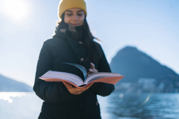 istock Young woman reads from book, by lakeshore 1359352304