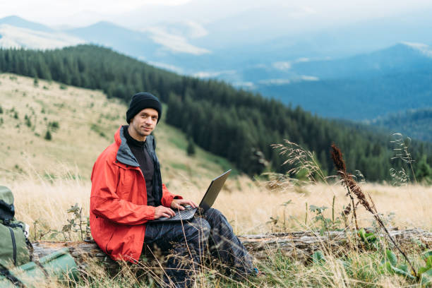 istock man working outdoors with laptop sitting in the mountains. Remote work or freelance lifestyle concept. Broadband cellular coverage. 5G Internet. Tourist tourist. 1359352392