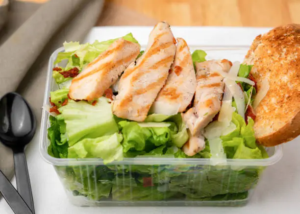 Chicken caesar salad with dressing in takeaway box