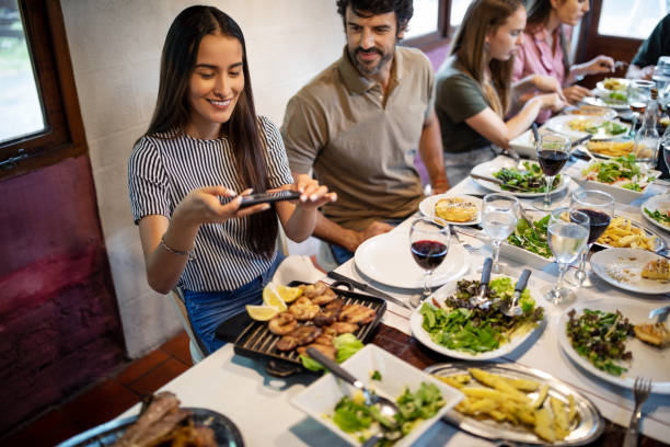 woman taking photos of a food with her mobile during family lunch - couple restaurant day south america imagens e fotografias de stock