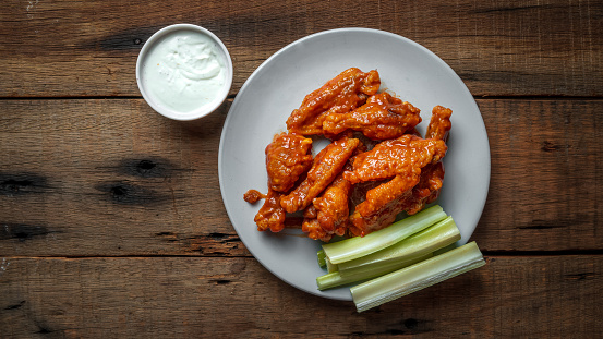 Traditionally spicy buffalo hot wings served with blue cheese sauce dip and celery on a wooden table