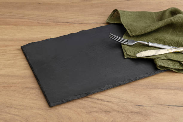 black slate board and fork,knife and green napkin on the wooden table.free space - focus on foreground eating utensil serving utensil tray imagens e fotografias de stock