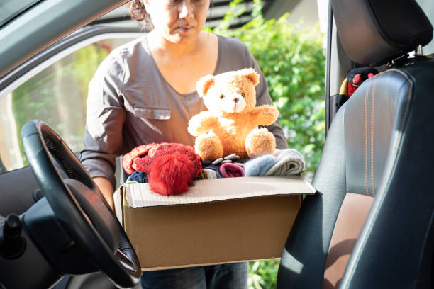 Volunteer woman provide clothing donation box with used clothes and doll in car to support help for refugee, homeless or poor people in the world. stock photo