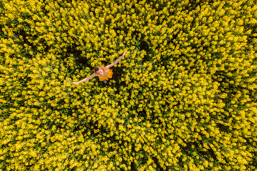 Woman in yellow dress at blooming rapeseed field. Bright yellow flowers and happy woman
