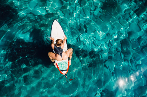 Surfer woman on surfboard wait wave in transparent ocean. Aerial view