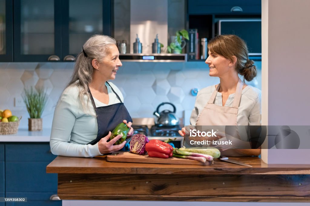 Caregiver and senior woman with vegetables at home Happy caregiver and senior talking at home. Elderly female and nurse are with vegetables. They are preparing food in kitchen. Preparing Food Stock Photo