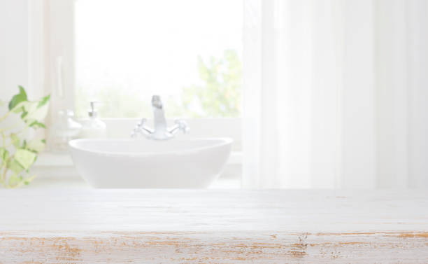 istock Wooden table top on blurred bathroom sink and curtained window 1359360150