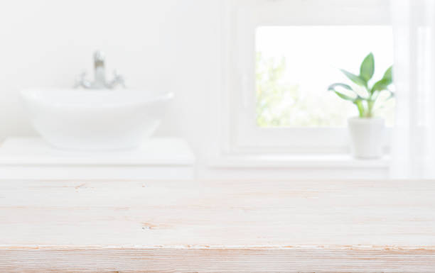 istock Old wooden tabletop on blur bathroom sink and window background 1359360230