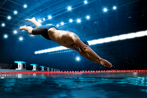 Professional young muscular swimmer jumping from starting block in a swimming pool