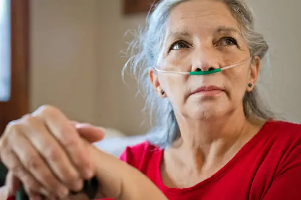 Close up of sad, grey hair senior woman receiving oxygen. Focus on foreground.