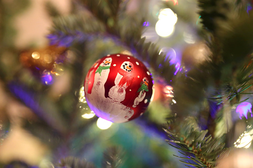 A handmade children's handprint snowman Christmas Ornament is hanging in the Christmas tree.