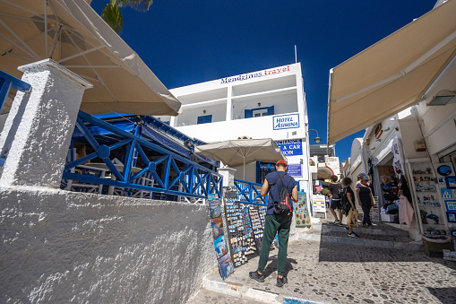 Tourist in Firá on Santorini in South Aegean Islands, Greece , with a gift shop, hotel and travel agency in the background