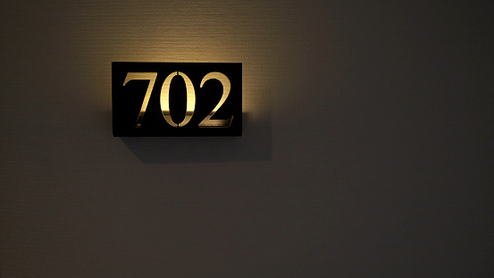 Room number 702 in apartment, hotel or office building. Sign plate indoors.