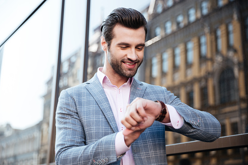 Portrait of a smiling young man checking the time on his wrist watch in a city area