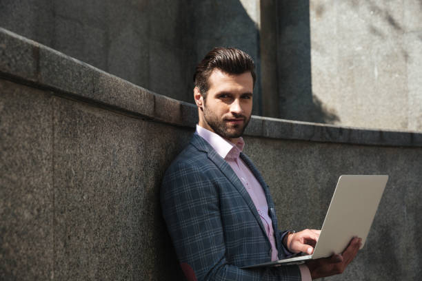 istock Portrait of young confident man in suit using laptop computer 1359373270