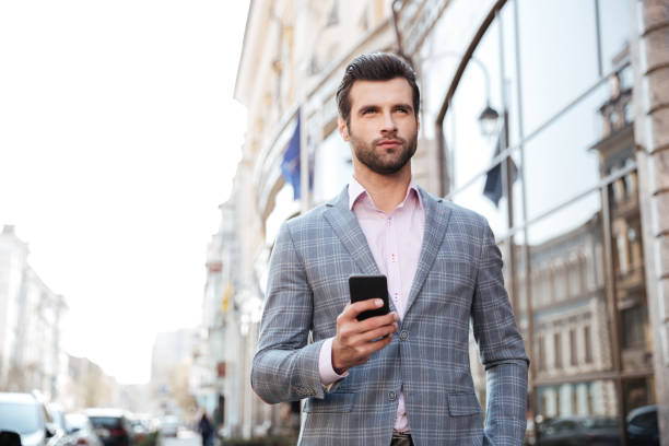 istock Handsome man in a jacket walking and holding mobile phone 1359374320