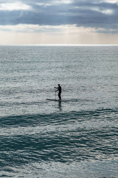 istock Unrecognizable person practicing paddle surfing Young athletic silhouette paddling stand up paddleboard. Healthy lifestyle. 1359375785