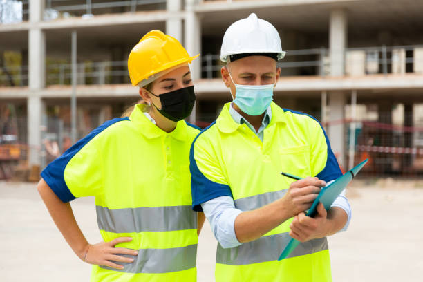 istock Man and woman engineers in face mask standing in construction site 1359376050