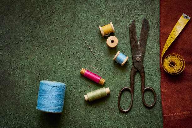 istock Old scissors, tailor tape and spools of thread on a dark green textured background close up, flat lay 1359379274