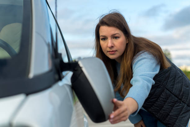 istock Broken off side rearview mirror on car. Woman is checking for damage on her auto 1359379382