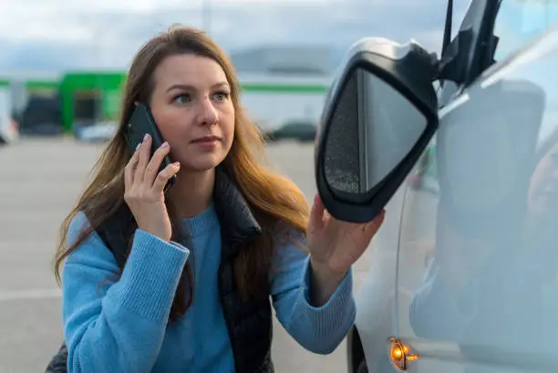 Photo of Woman speaks on phone. Traffic accident with car, broken off rear-view mirror