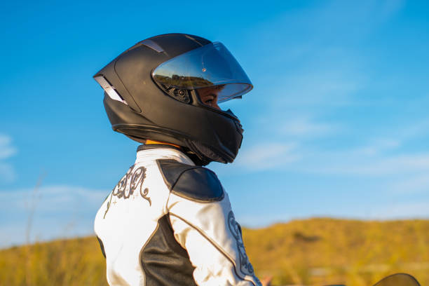 istock young biker woman in profile dressed in white patterned jacket and black safety helmet. blue sky background 1359381463