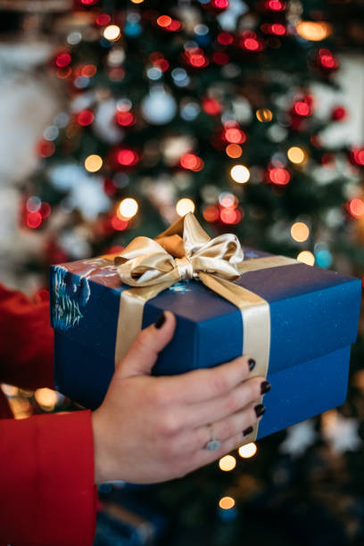 istock Woman holding gift box in front of christmas tree 1359396310