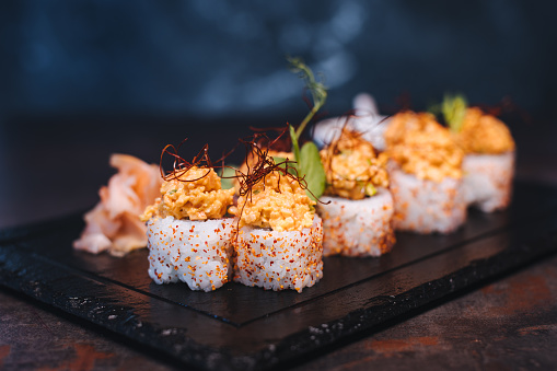 Set of sushi rolls with cream cheese, rice and salmon on a black board decorated with soy sauce and avocado on a dark wooden background. Japanese cuisine. Food photo background