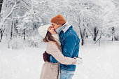 Young loving couple kissing in winter park. Man and woman hugging enjoying snowy landscape outdoors