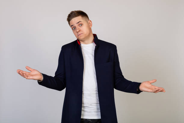 male young man with a lost expression shrugs his shoulders. the guy spreads his hands and does not know what to say in response - blank expression head and shoulders horizontal studio shot imagens e fotografias de stock