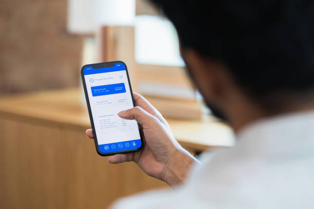 Over the shoulder view unrecognizable man using online banking app An over the shoulder photo of an unrecognizable man using an online banking app on his smart phone. man looking at phone over shoulder stock pictures, royalty-free photos & images