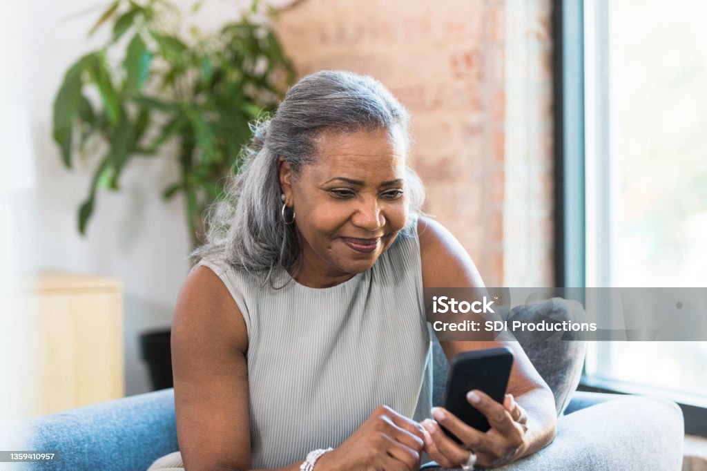 Taking a break from work, business woman surfs net Taking a break from work, the senior adult businesswoman enjoys surfing the net on her smart phone. Using Phone Stock Photo
