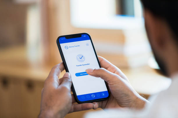 Close up photo man holding phone with banking app A close up photo of an unrecognizable man holding his smart phone with a banking app displayed on the screen. man looking at phone over shoulder stock pictures, royalty-free photos & images