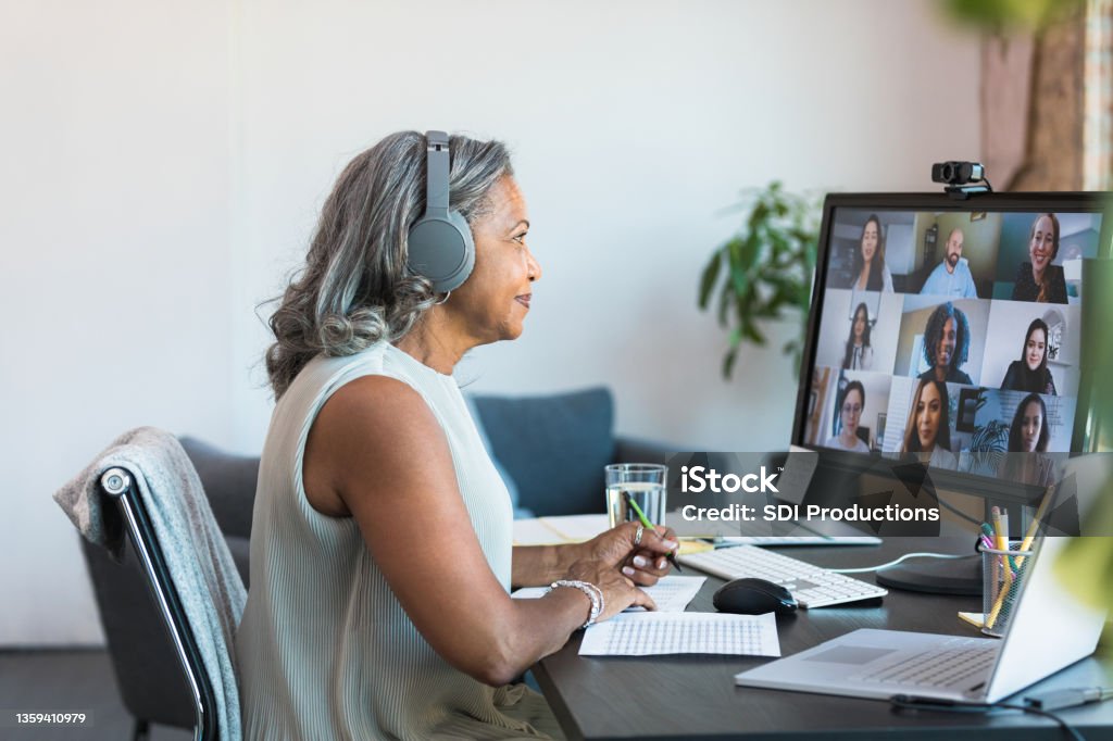 Senior CEO leads meeting with employees from home The senior adult female CEO leads a meeting with her employees from her home office.  She is taking notes on the spreadsheet and has her laptop open. Video Call Stock Photo