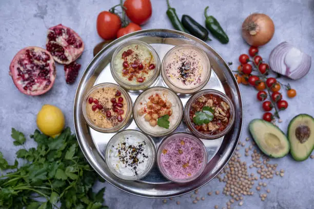 A tabletop view of a metal tray filled with small plates of mezes, half a pomegranate, onion, tomatoes, avocado, pepper and a bunch of parsley seen blurry on the table.