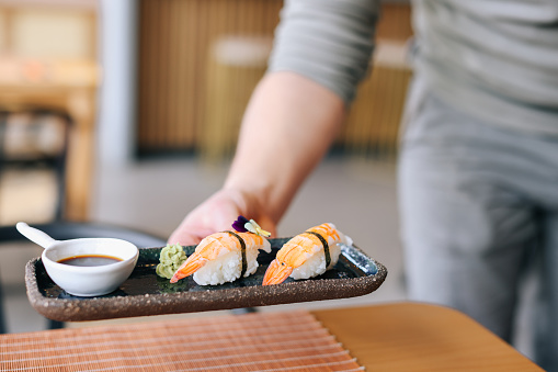 Waiter holding a set of sushi rolls on a white plate. Close-up, selective focus