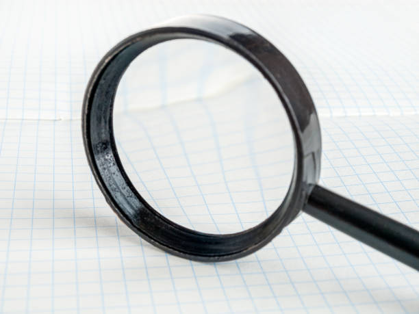istock Magnifying glass on the background of a notebook in a cage, reading small text, selective 1359413676