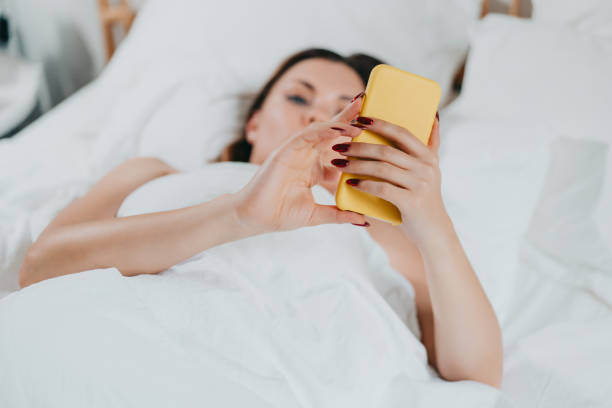istock Woman holds smartphone in hands while lying in comfortable bed. Lady with mobile in light cozy bedroom. Addiction to technology and social media, morning rituals concept. 1359416987
