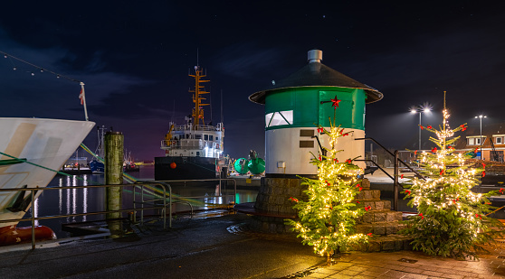 Green pier light and cristmas trees in the fishing port of Büsum on the German North Sea coast, Dithmarschen, Schleswig-Holstein, Germany. Christmas romantic atmosphere in the Büsum at night.