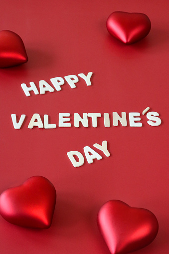 Stock photo showing elevated view of red background with white lettering, Valentine's Day greeting card sign with red 3D hearts.
