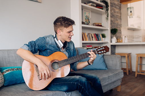 Young man enjoying at his living room and playing a guitar.