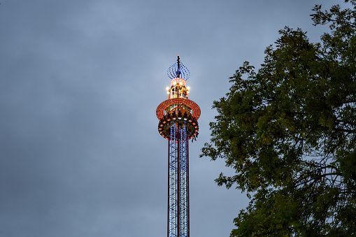 Dresden, Fairground ride very high in the air in front of a dark sky. The illuminated free fall tower is waiting at the upper position and making people afraid.