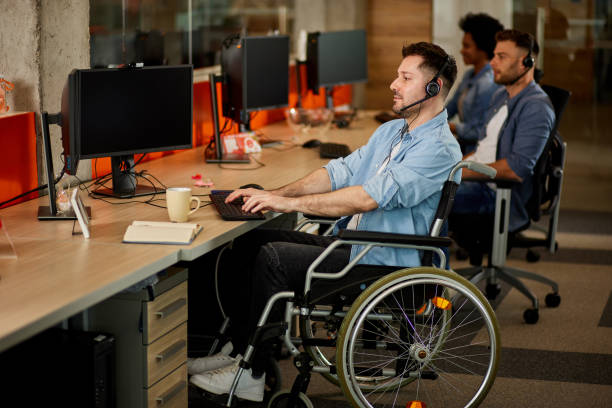 istock Handicapped computer programmer in wheelchair at his office desk 1359443382