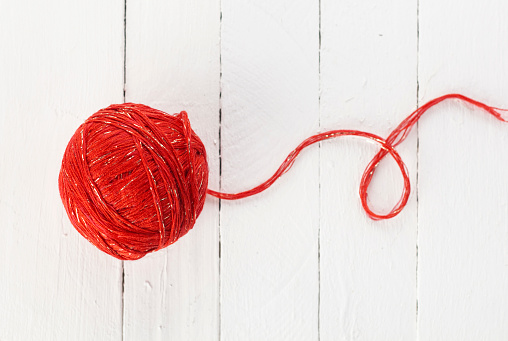 a ball of red yarn on a white background of painted boards.