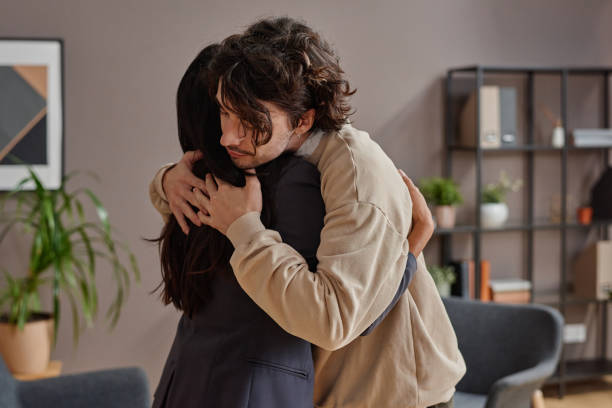 istock Horizontal medium shot of young man suffering depression getting support from professional psychologist hugging her 1359467137