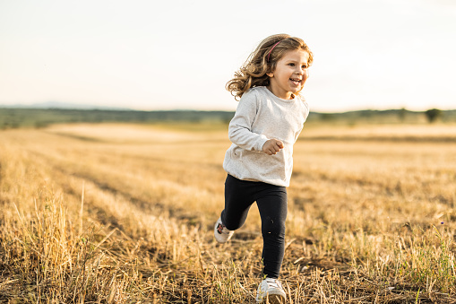 Cute little smiling girl running in nature over grass field