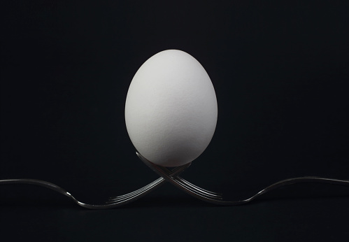 Egg on two forks on black background